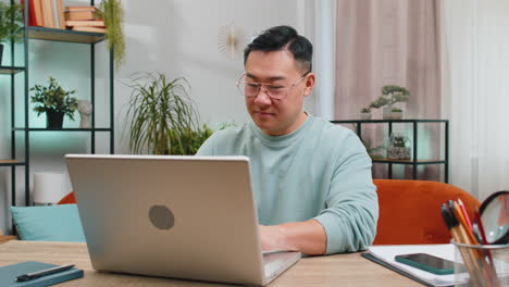 confident concentrated asian man working remotely on a project on laptop computer at home room