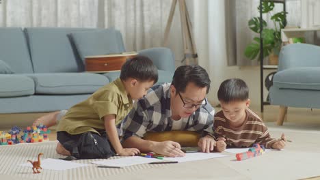 full body of asian father and sons on the floor in the room with plastic toy brick. looking at smartphone, drawing, talking, playing together at home