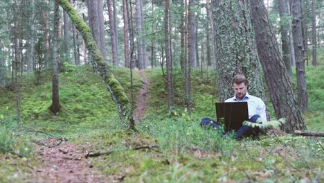 young businessman working on laptop under the tree in the forest