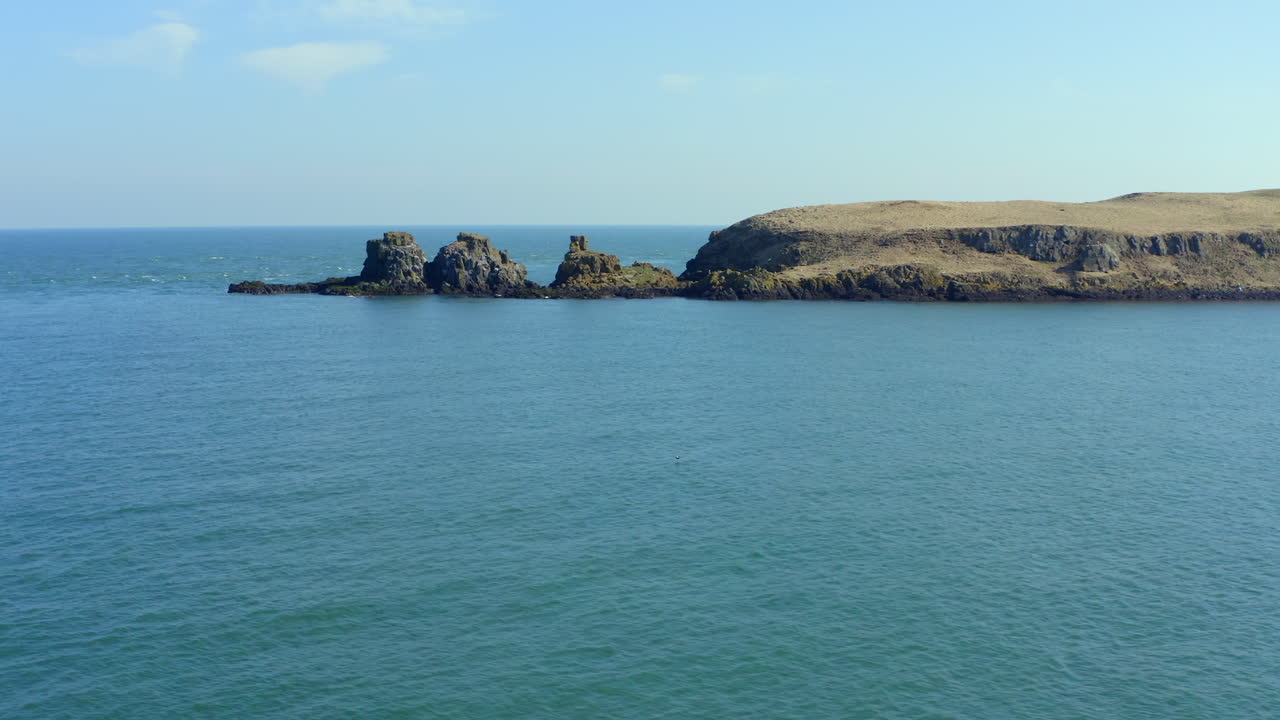 Drone moving sideways past Portmuck's rocky coastline before revealing expansive blue sea