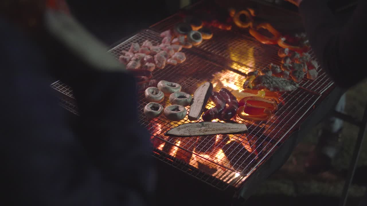 정원에 있는 집 앞 바비큐에서 버섯, 소시지, 닭고기, 가지를 굽는 사람들의 어깨 뒤에서 보기