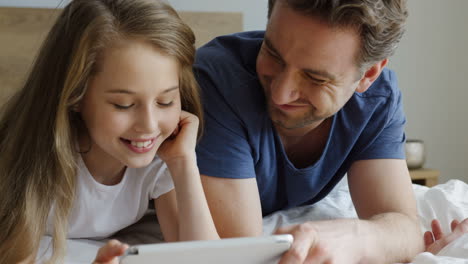 close-up view of a little girl and her father lying on the bed and watching something on the tablet