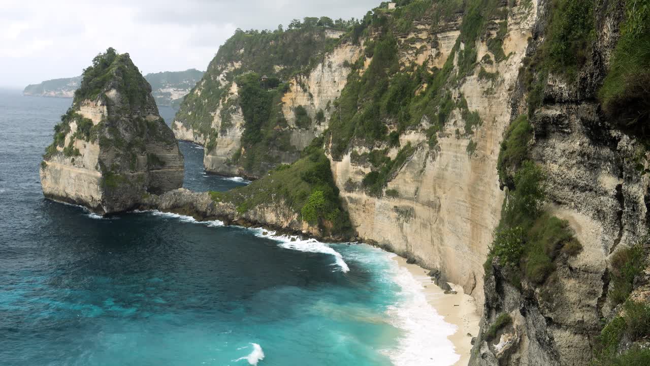 arriba disparado frente a los acantilados de nusa penida con vistas a la hermosa playa de diamantes mientras las olas del mar azul lavan la playa