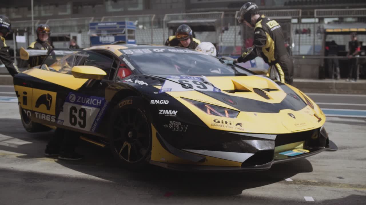 Pit crew mechanics preparing and cleaning Giti Lamborghini Huracan race car in pit lane in sunny daylight before the start of the ADAC Nurburgring twentyfour hour race.