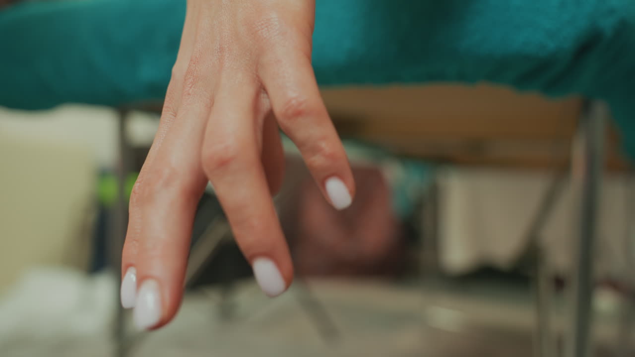 closeup client hand on teal towel during microcurrent massage, white nail polish, subtle finger movement, therapist blurred in background, clinical spa room with soft lighting and calm atmosphere
