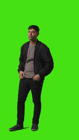 vertical video full length shot of casually dressed young man standing against green screen putting hands in pockets