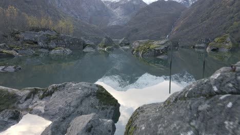 rocks in majestic mountain lake with snowy peek reflection in water, dolly forward tilt up shot