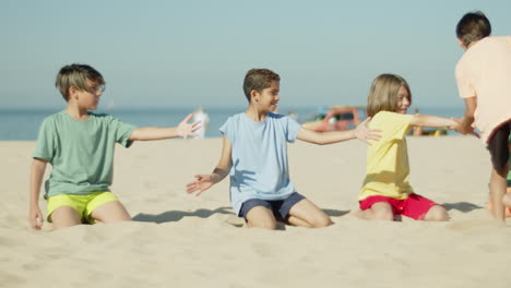 Junge-Rennt-Und-Gibt-Fünf-An-Freunde,-Die-Am-Sandstrand-Sitzen