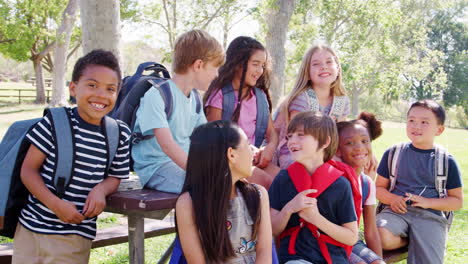 Group-Of-Children-With-Friends-In-Park-Sitting-Around-Table-Shot-In-Slow-Motion