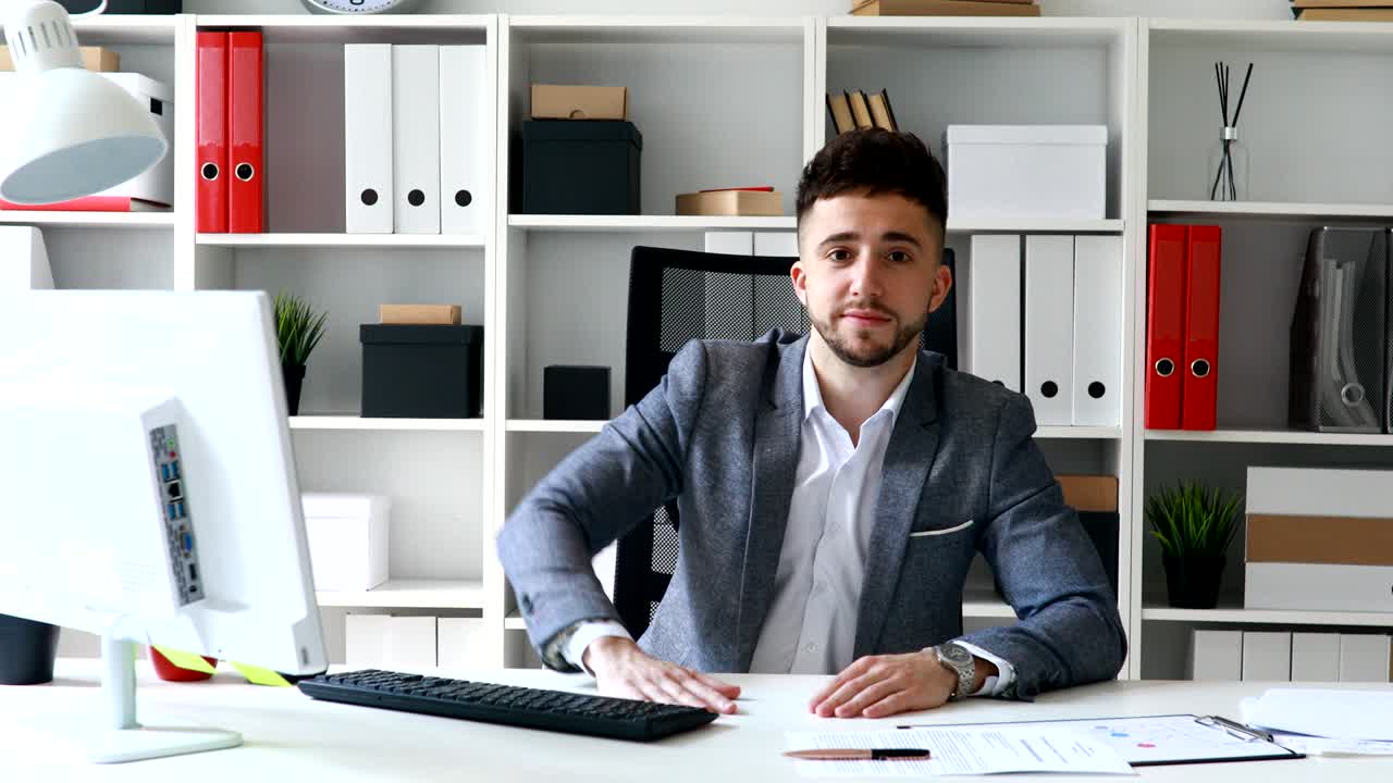 uomo d'affari in giacca grigia seduto a tavolo in un ufficio bianco e che offre documenti