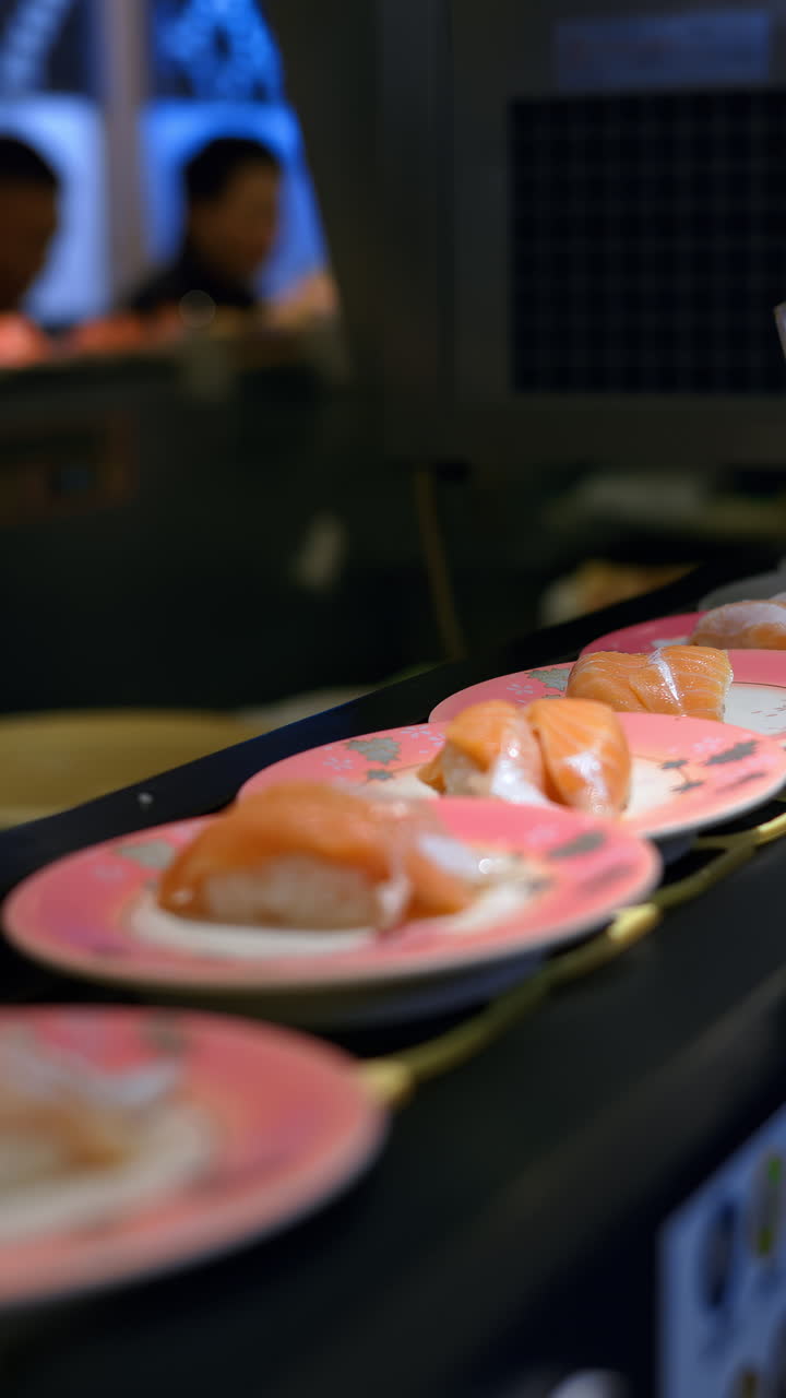 Close up of plates with sushi placed on a rotating conveyor belt moving through the restaurant. Vertical