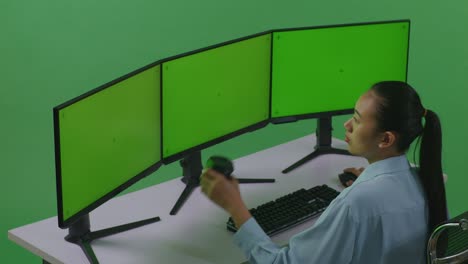 vista lateral de una mujer asiática bebiendo café y trabajando con un simulacro de múltiples monitores de computadora en un estudio de pantalla verde