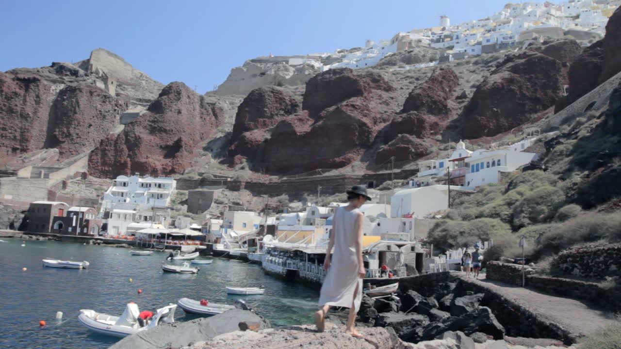 vista de un pequeño puerto pesquero en una isla griega con una mujer que pasea por las rocas