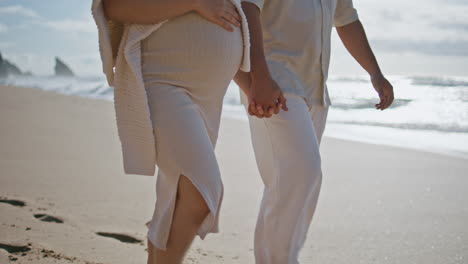 pair legs walking beach near ocean waves closeup. pregnant couple relaxing sea