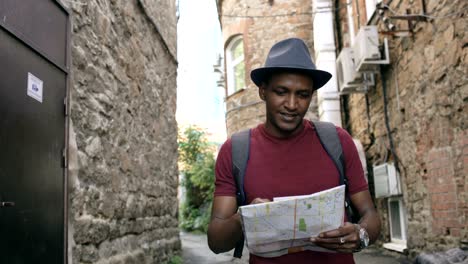 steadicam shot of african american tourist man walking and watching paper city map to find directions to famous place