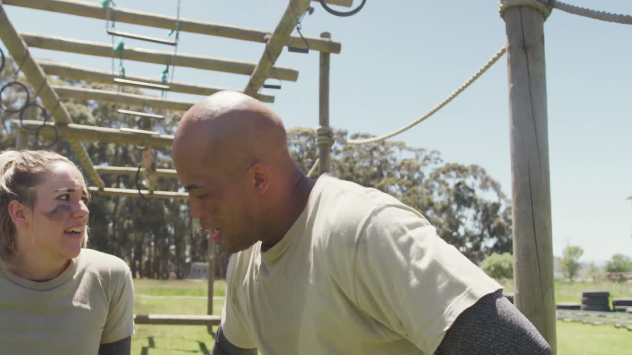cansado, diverso soldado masculino y femenino descansando en el curso de obstáculos del ejército en el sol