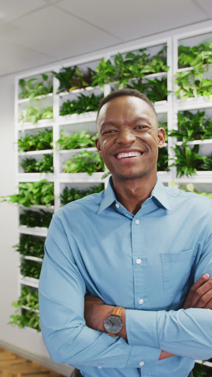Vertical video of portrait of happy african american businessman smiling at office