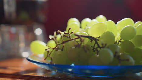 close up of fresh green grapes on blue glass plate, resting on wooden table under soft natural light, background softly blurred with bokeh
