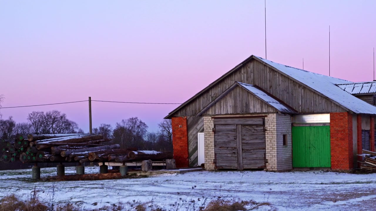 Rustic old barn with stacked lumber logs resting in the serene winter countryside at dawn