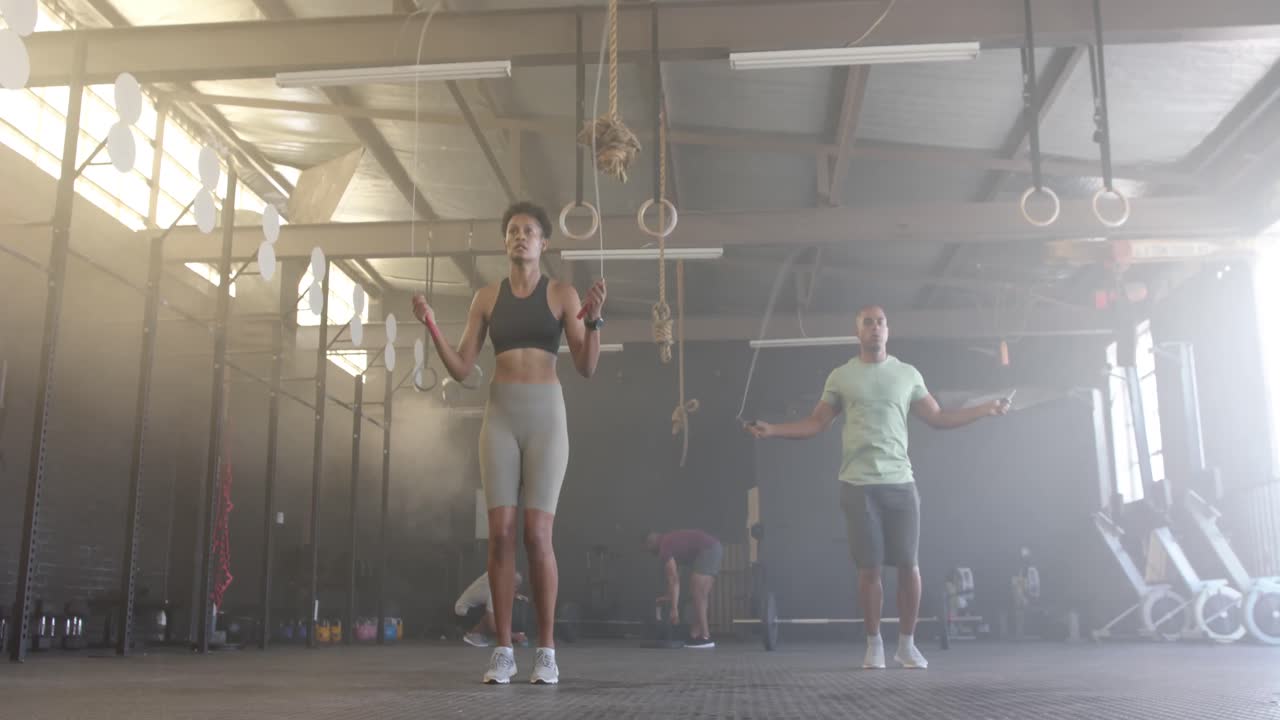hombre y mujer diversos entrenando en el gimnasio saltando la cuerda, en cámara lenta