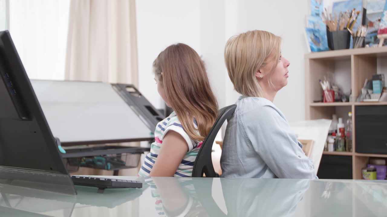 Mother and daughter sitting back-to-back at desk