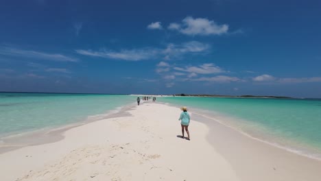 Woman-walks-on-white-sand-beach-and-puts-on-shoes-to-continue-on-tropical-sandbank,-turquoise-sea-water-splash,-cayo-de-agua