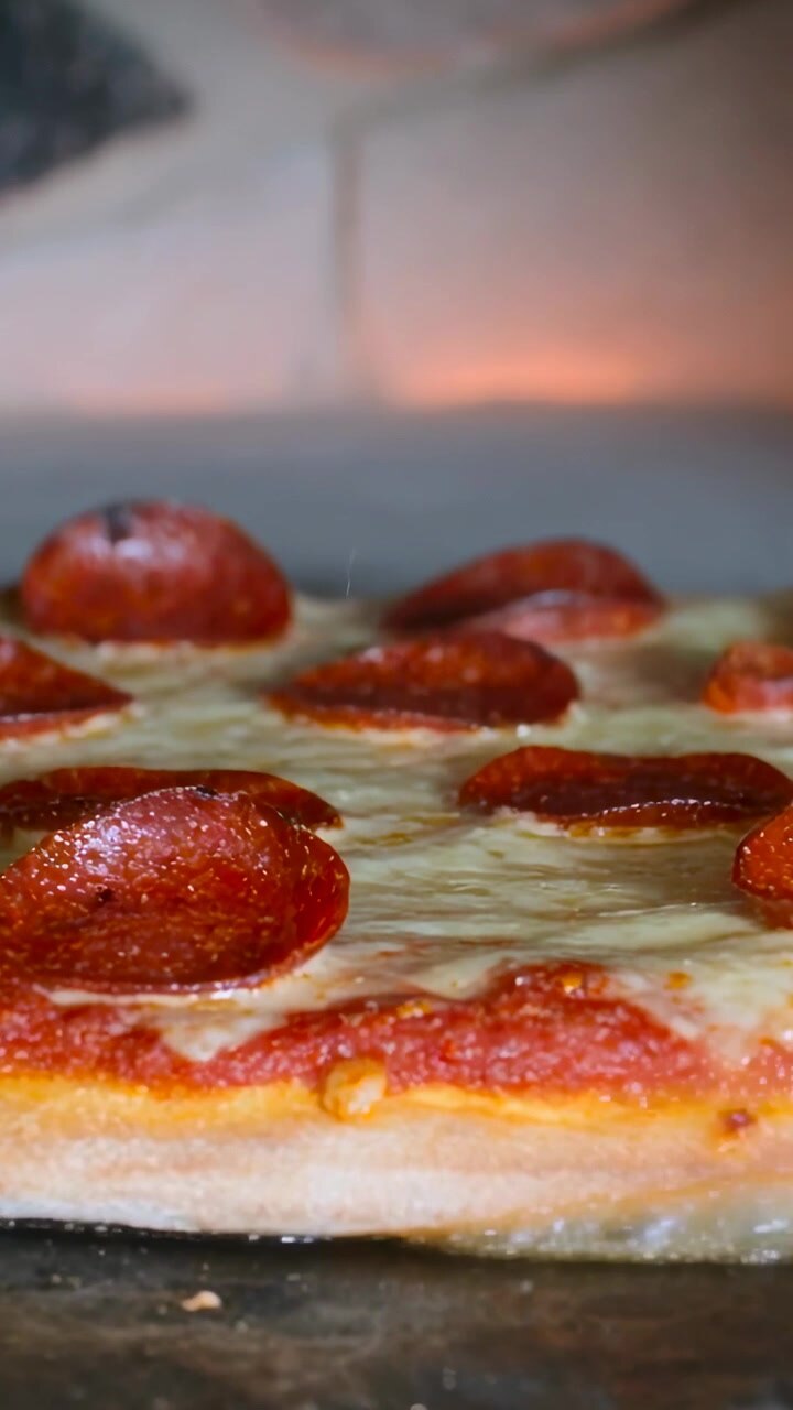 Video verticale: Posizionare la pizza su pietra calda nel forno per la cottura, con il salame piccante che si arriccia e il formaggio che si scioglie.