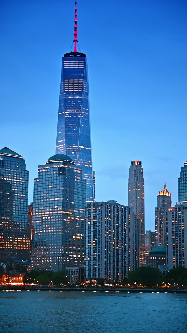 Belos arranha-céus e edifícios altos de Nova York com luzes acesas nas janelas. Skyline da metrópole da paisagem aquática ao anoitecer. Vídeo vertical