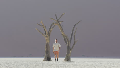joven fotógrafo con cámara caminando en medio de árboles camelthorn muertos en deadvlei