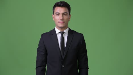 young handsome hispanic businessman against green background