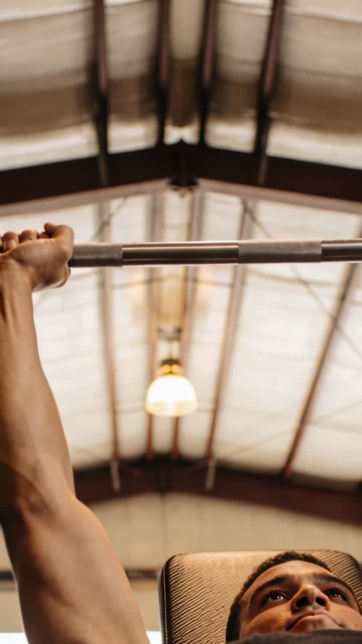 Vertical video: Grip tightening man in tank top pressing barbell on bench in gym, for workout