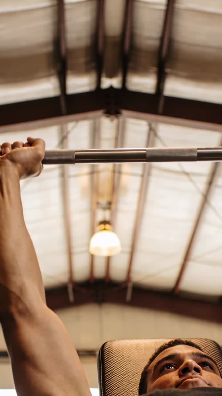 Vertical video: Grip tightening man in tank top pressing barbell on bench in gym, for workout