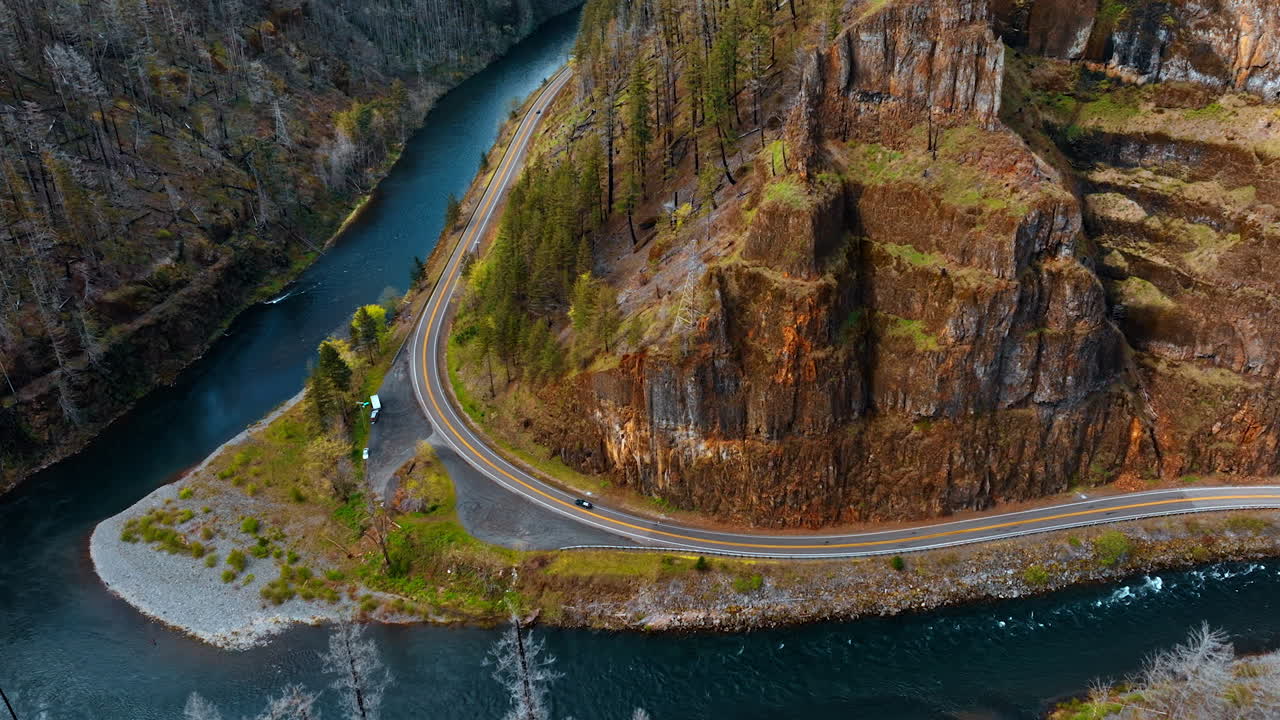 Wavy highway built around the bare rocks in Oregon State, USA. Beautiful narrow river flows at the foot of the mountains. Top view.