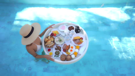 top down view of wealthy female in swimming pool with floating breakfast plate