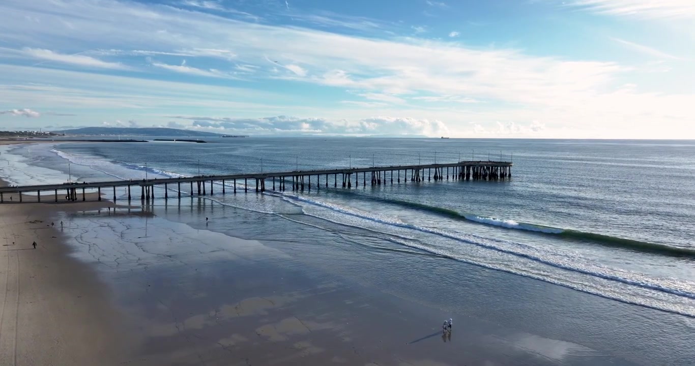 Una ripresa aerea cinematografica grandangolare con drone del molo di Santa Monica, che si protende lontano da Venice Beach, ruotando lentamente in avanti sopra la costa del Pacifico a Los Angeles, California.