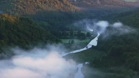 aerial view of a river flowing through a forest in a valley with fog