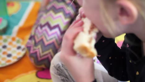 a young female girl caucasian white child is eating a peanut butter and jelly sandwich with another kid in the background