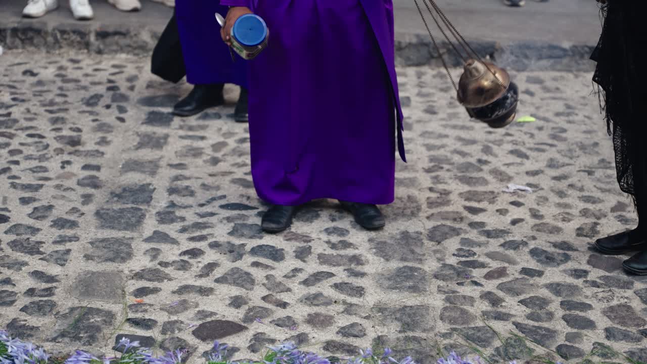 Close-up of a participant in purple robes carrying an incense burner on cobblestone streets during Semana Santa in Antigua Guatemala.