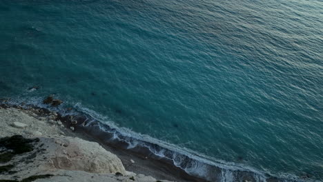 steep cliff overlooking the deep blue waters of the mediterranean sea, with waves gently crashing against the rocky shore