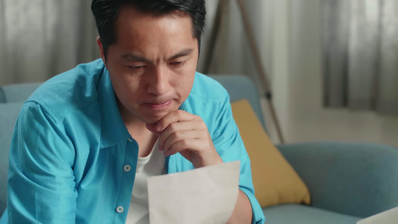 집에서 노트북으로 일하기 전에 청구서를 보고 생각하는 아시아 남자의 클로즈업
