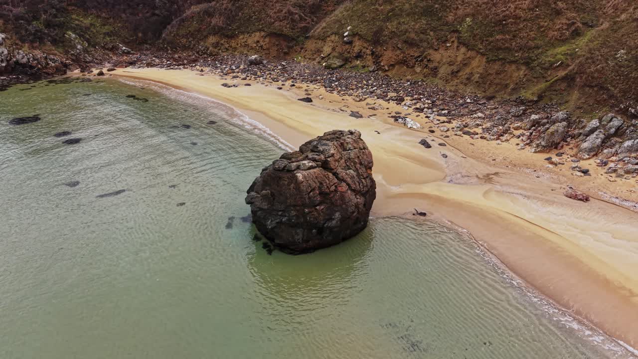 Grande roccia su una spiaggia sabbiosa vicino ad acque calme sotto un cielo nuvoloso