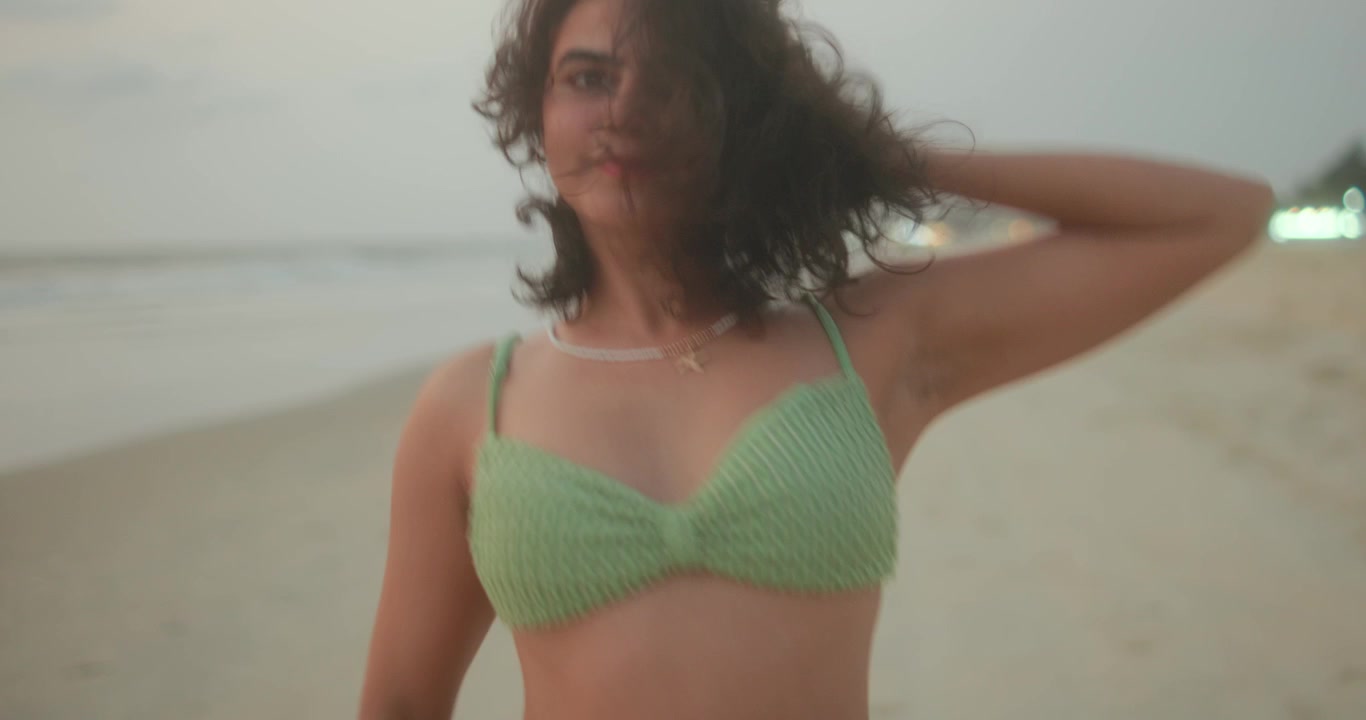 Een jonge vrouw danst op een tropisch strand in een groene bikini, met wild haar en stralende energie