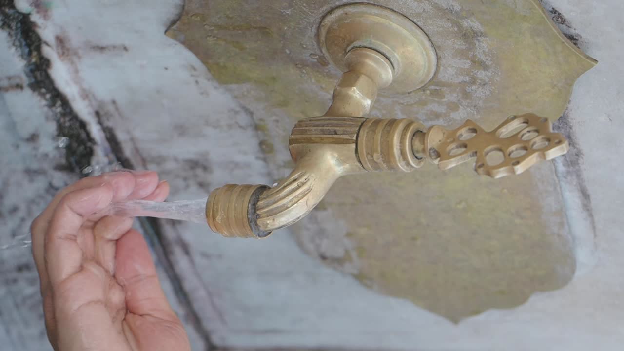 Close-up of a faucet with running water and a hand