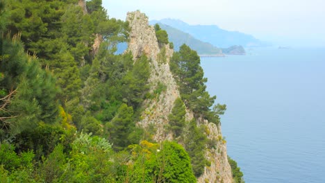 Overlooking-coastline,-landscape-and-sea-with-rocky-cliffs,-blue-water-and-mountains-in-the-background-in-Capri-island,-Italy