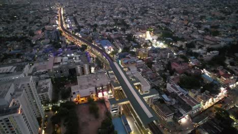 Una-Vista-Aérea-De-La-Ajetreada-Zona-De-Señales-De-Vadapalani-De-La-Ciudad-De-Chennai-Tomada-Por-La-Noche-Muestra-El-Metro-En-Movimiento,-Las-Calles-Congestionadas,-Los-Edificios-De-Apartamentos-Y-La-Estación-De-Metro