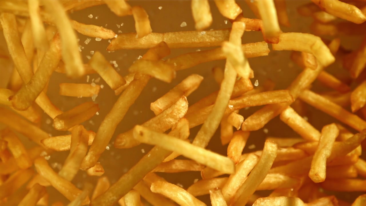 Primer plano de sal cayendo sobre patatas fritas doradas