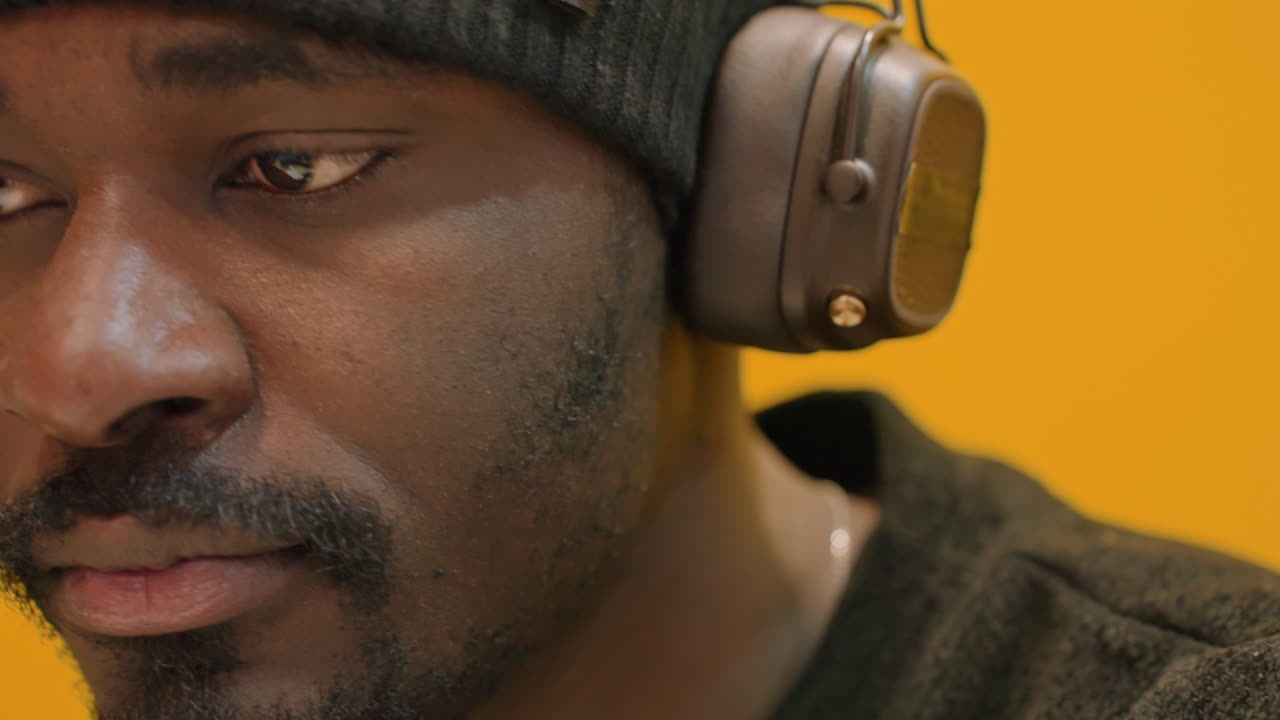 Uomo che controlla le cuffie durante il mix finale, postura da ingegnere del suono con ascolto concentrato, espressione sicura, sfondo giallo dello studio, primo piano dell'attrezzatura, illuminazione calda, momento di approvazione del mastering.