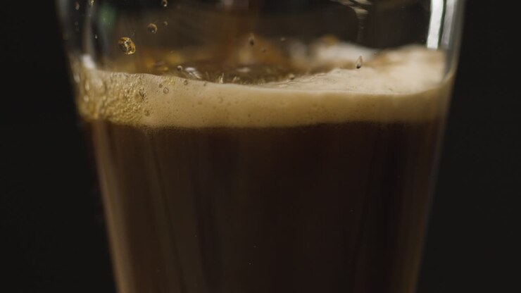 Pinta di birra stout irlandese versata in un bicchiere su sfondo nero in studio per celebrare il Giorno di San Patrizio 1
