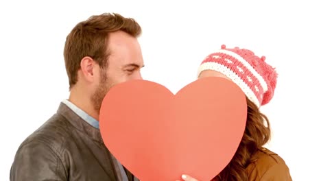 una joven pareja cubriendo su cara con un corazón de almohada