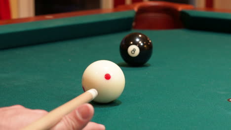 closeup of person playing pool shooting solid black 8 ball into corner pocket after practice strokes using cue ball with red spots, open bridge hand with wooden cue stick and green felt or cloth